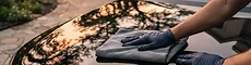 A glossy black car being hand-detailed in a driveway at golden hour
