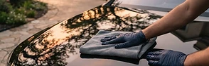 A glossy black car being hand-detailed in a driveway at golden hour