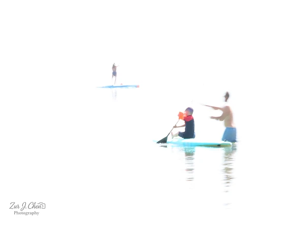 צילום אמנותי בעל אופי מופשט המתעד אנשים על גבי גלשני סאפ בלב ים. השימוש בערכי חשיפה קיצוניים יוצר רקע לבן ובוהק, המעניק לדמויות מראה אוורירי ומרחף. טשטוש מכוון בשילוב עם תאורה חזקה מטשטשים את גבולות המים והשמיים, ויוצרים תחושת שקט, ניקיון חזותי ומינימליזם מרתק בתוך מרחב ימי פתוח.