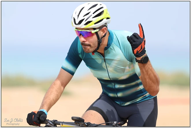 צילום ספורט דינמי המתעד רוכב אופניים תוך כדי רכיבה. הצלם השתמש בעומק שדה רדוד שמטשטש את הרקע, מה שמדגיש את הרוכב ואת הבעת הריכוז שלו. התאורה הבהירה והקומפוזיציה הממוקדת מעניקות לתמונה תחושת אנרגיה ותנועה, כאשר הצבעים בחולצת הרכיבה משתלבים בהרמוניה עם האווירה הכללית של האירוע.