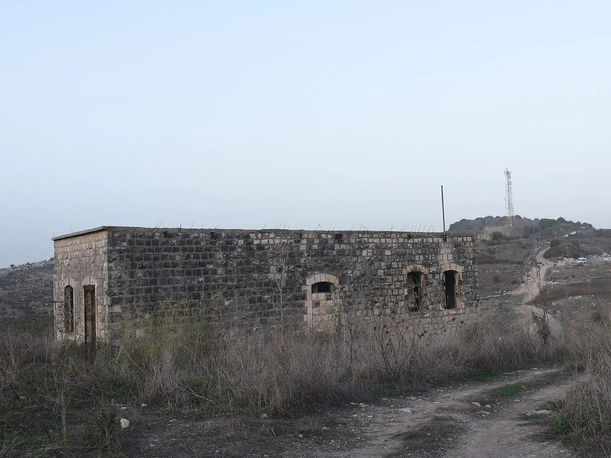 צילום נוף המציג מבנה אבן עתיק ונטוש הניצב בלב שטח פתוח וצחיח למחצה. קומפוזיציית הצילום משלבת בין המבנה לדרך עפר מפותלת המובילה אל עבר אופק רחוק, תחת שמיים בהירים ושטוחים. שימוש בעדשה רחבה (18 מ"מ) מדגיש את תחושת המרחב, בעוד תאורת היום הרכה מדגישה את הטקסטורה המחוספסת של האבנים הישנות.