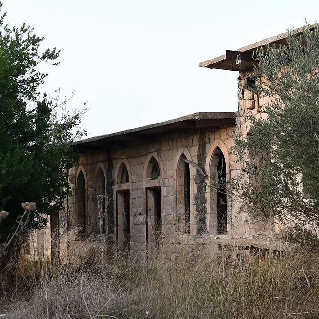 בתמונה נראה מבנה אבן עתיק ונטוש בעל קשתות מחודדות המשתלב בנוף כפרי. הצילום שבוצע בעזרת עדשת 35 מ"מ, מדגיש את הטקסטורה של אבני המבנה ואת הצמחייה הפראית הסובבת אותו. תאורה רכה מלטפת את החזית, בעוד עומק השדה מפריד יפה בין אלמנטים קדמיים של קוצים לבין המבנה ההיסטורי המרשים בדרכו.