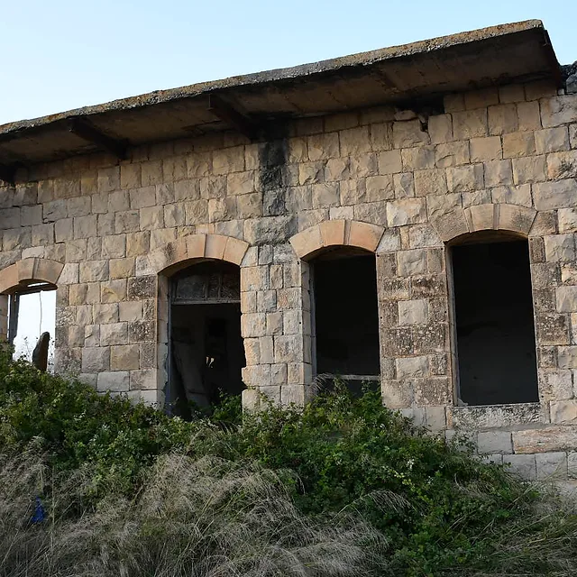 צילום דוקומנטרי מרתק של מבנה אבן עתיק ונטוש, המתאפיין באדריכלות כפרית קלאסית. המבנה מוקף צמחייה פראית המשתלטת על חזיתו, מה שמעניק לו מראה נוסטלגי ומסתורי. התאורה הרכה בשעות אחר הצהריים מחמיאה למרקם האבן המחוספס, בעוד שעדשת ה-18 מ"מ תופסת קומפוזיציה רחבה המדגישה את בדידות המבנה בלב הסביבה הטבעית.
