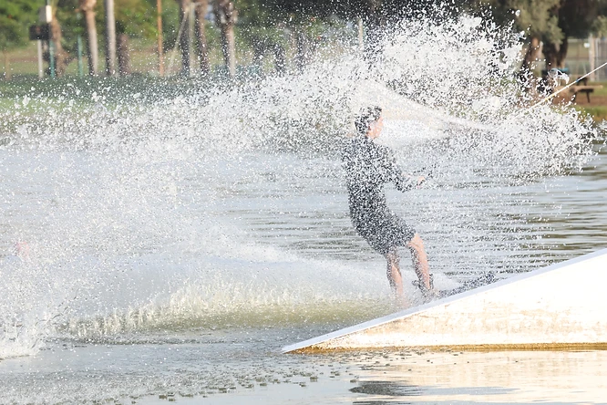 ספורטאי גולש על מים בביצוע תמרון מרהיב ב-LAKE- TLV פארק דרום תל אביב, כשהוא מוקף בהתזות רסס דרמטיות. השימוש במהירות תריס גבוהה של 1/5000 שניות הקפיא את טיפות המים בדיוק רב, בעוד הקומפוזיציה מדגישה את הדינמיות של הרגע ואת האינטראקציה העוצמתית של הגולש עם המים והמתקן.