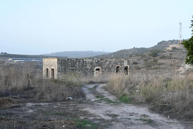 צילום נוף המציג מבנה אבן עתיק ונטוש הניצב בלב שטח פתוח וצחיח. הקומפוזיציה הרחבה, שצולמה במוקד 26 מ"מ, מדגישה את הבדידות של המבנה על רקע גבעות מרוחקות. התאורה הטבעית הרכה מעניקה למבנה מראה היסטורי, בעוד הצבעוניות המונוכרומטית והטקסטורה של אבני הבנייה יוצרות אווירה דוקומנטרית שקטה ונוסטלגית.