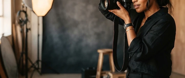 A professional portrait photographer at work with a camera in a warm, softly lit studio