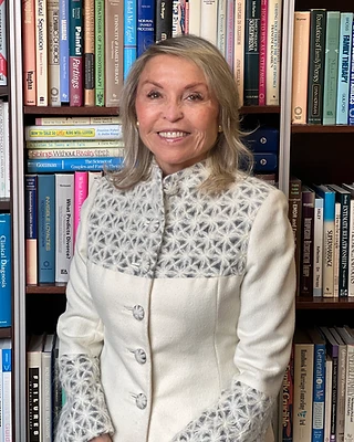Dr. Lilli Friedland standing before a bookshelf of clinical and family therapy texts in her Beverly Hills office.