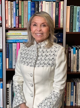 Dr. Lilli Friedland standing before a bookshelf of clinical and family therapy texts in her Beverly Hills office.