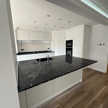 Modern kitchen with dark stone island and white handleless cabinetry, UC-Homes.