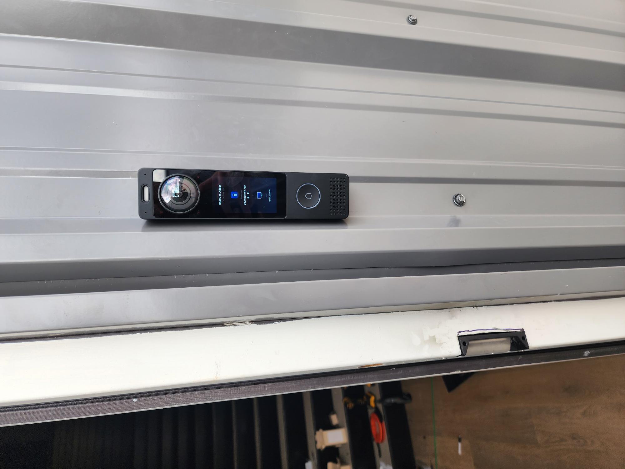 UniFi Protect video intercom mounted on corrugated metal siding, displaying a ready-to-adopt screen with camera, display, and call button