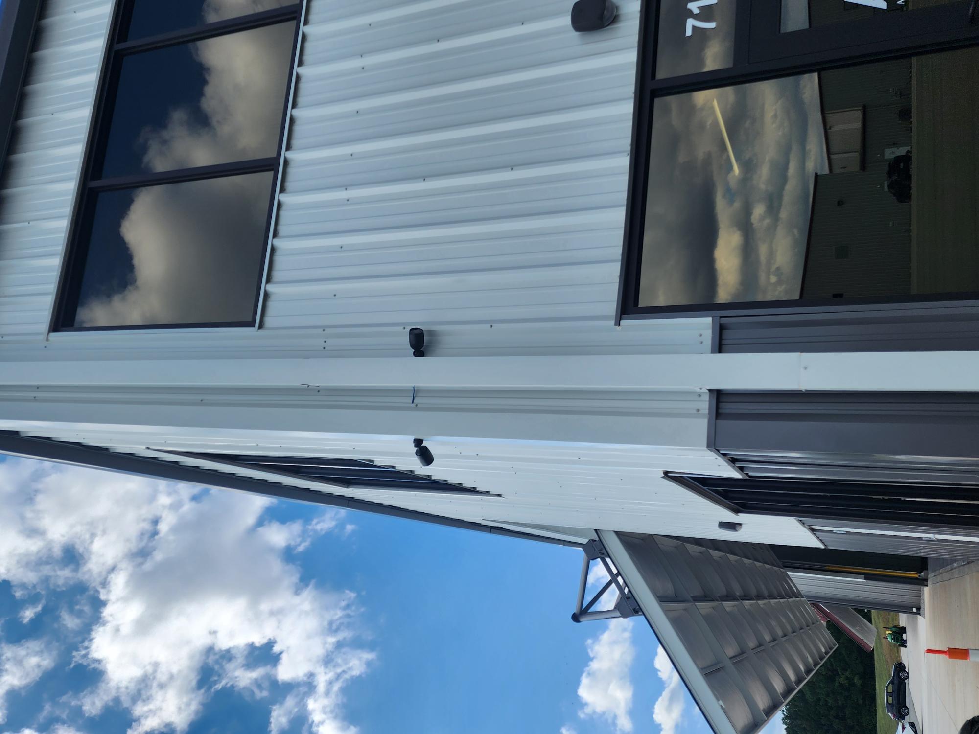 Exterior of a corrugated metal building with two black security cameras mounted vertically on the white siding