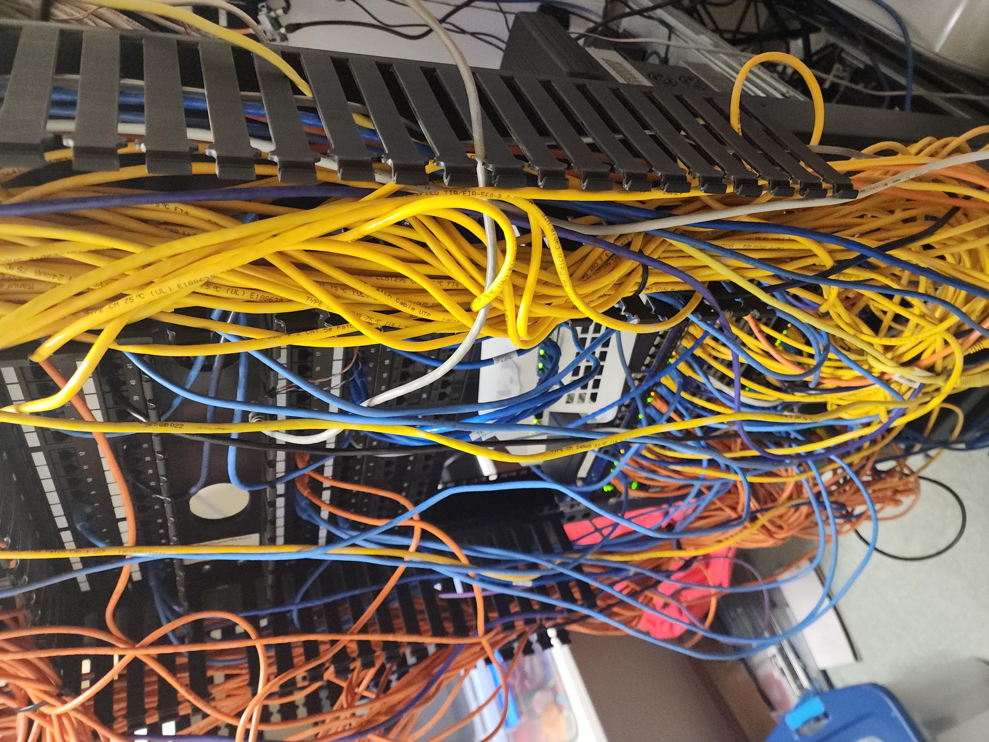 Network rack before cleanup, cluttered with a tangled web of yellow, blue, and orange Ethernet patch cables