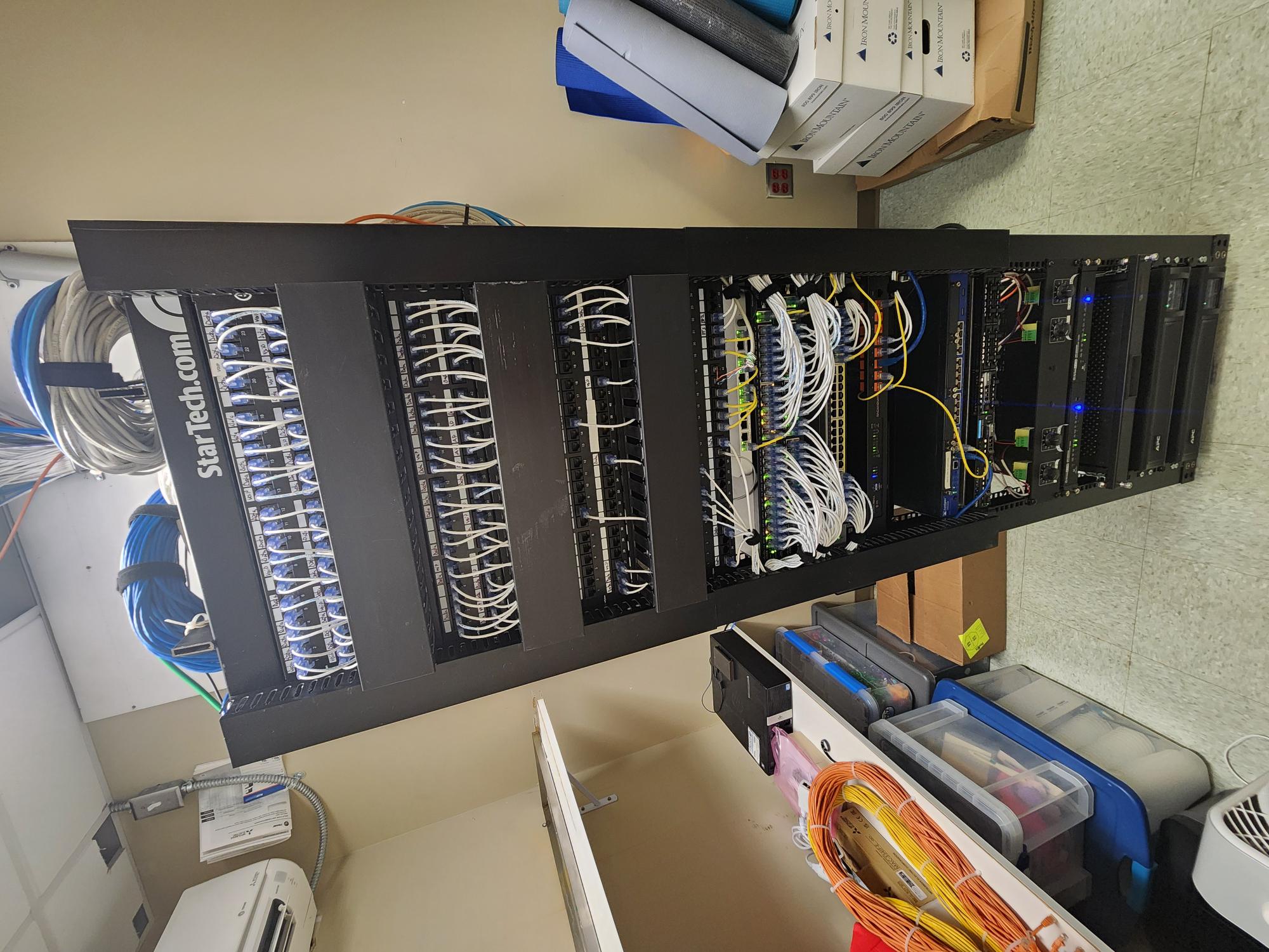 Finished StarTech wall-mounted rack with patch panels and switches, white patch cables dressed through management channels and bundles secured with Velcro straps