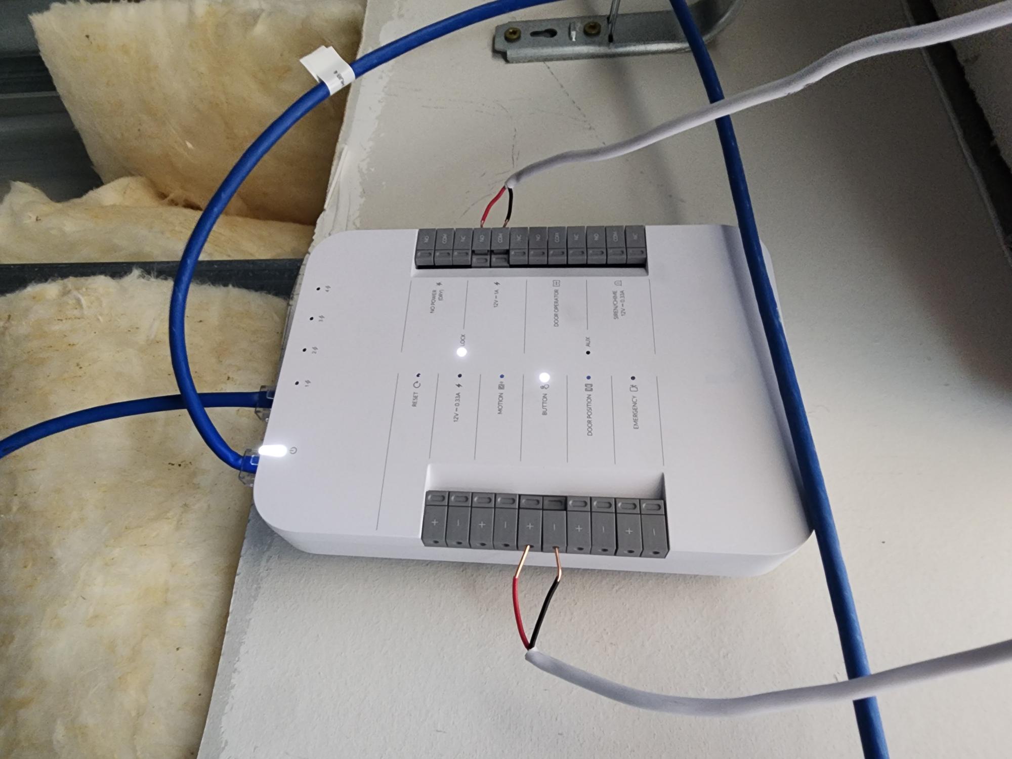 White access hub controller mounted on a wall with blue Ethernet cables, red and black power wiring, and labeled LED status indicators