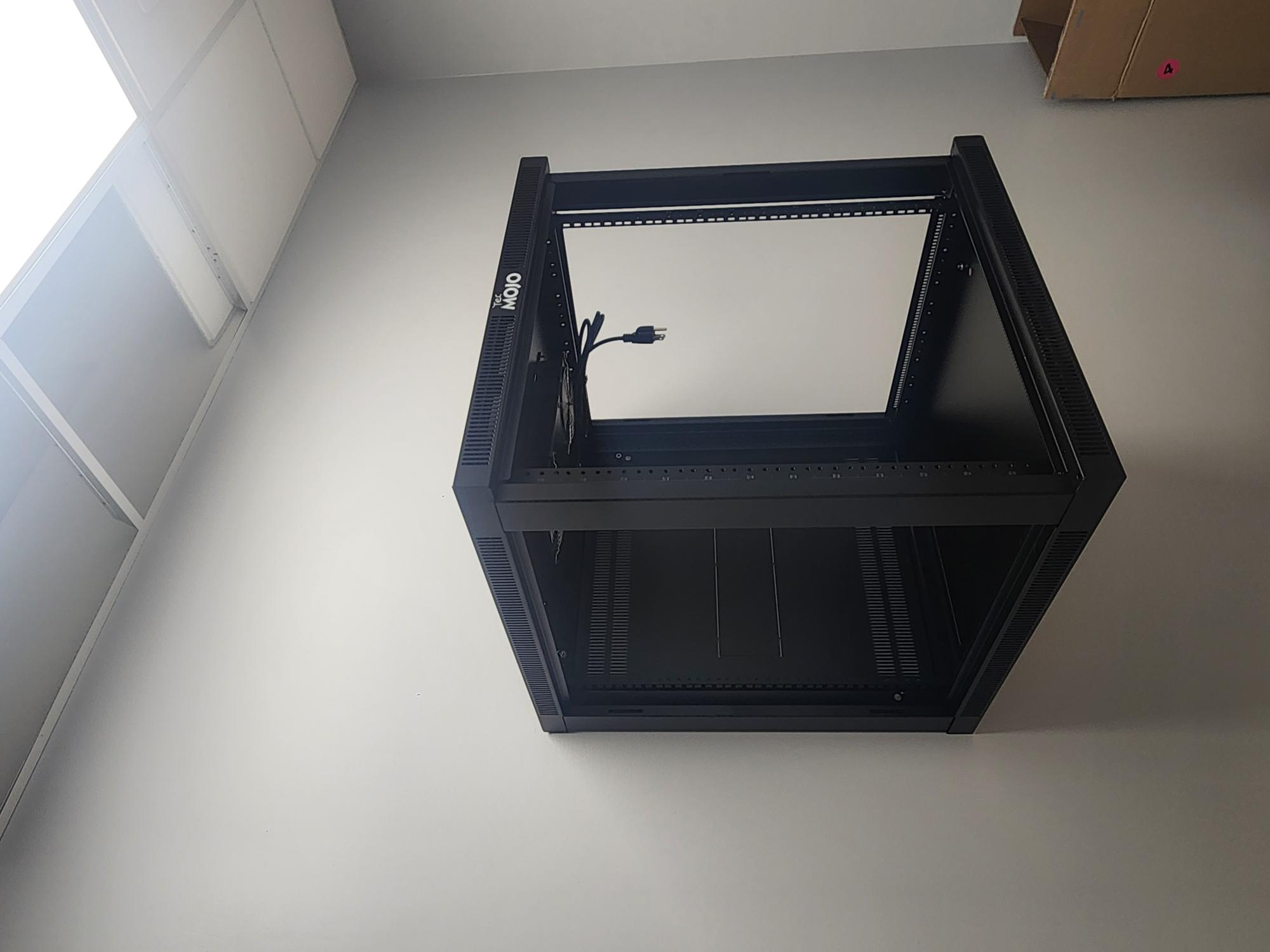 Empty black wall-mounted TecMOJO server rack with open frame and mounting rails against a light grey wall