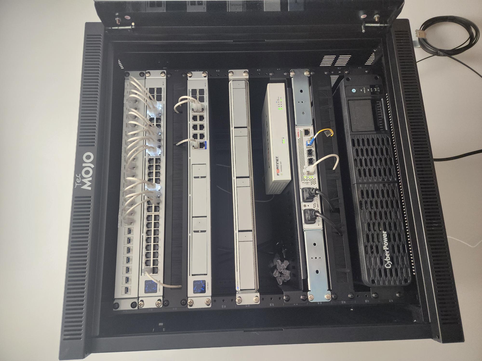 Open TecMOJO network rack interior with Ubiquiti switch and gateway, Fortinet firewall, Ciena interface unit, and CyberPower UPS with white patch cables