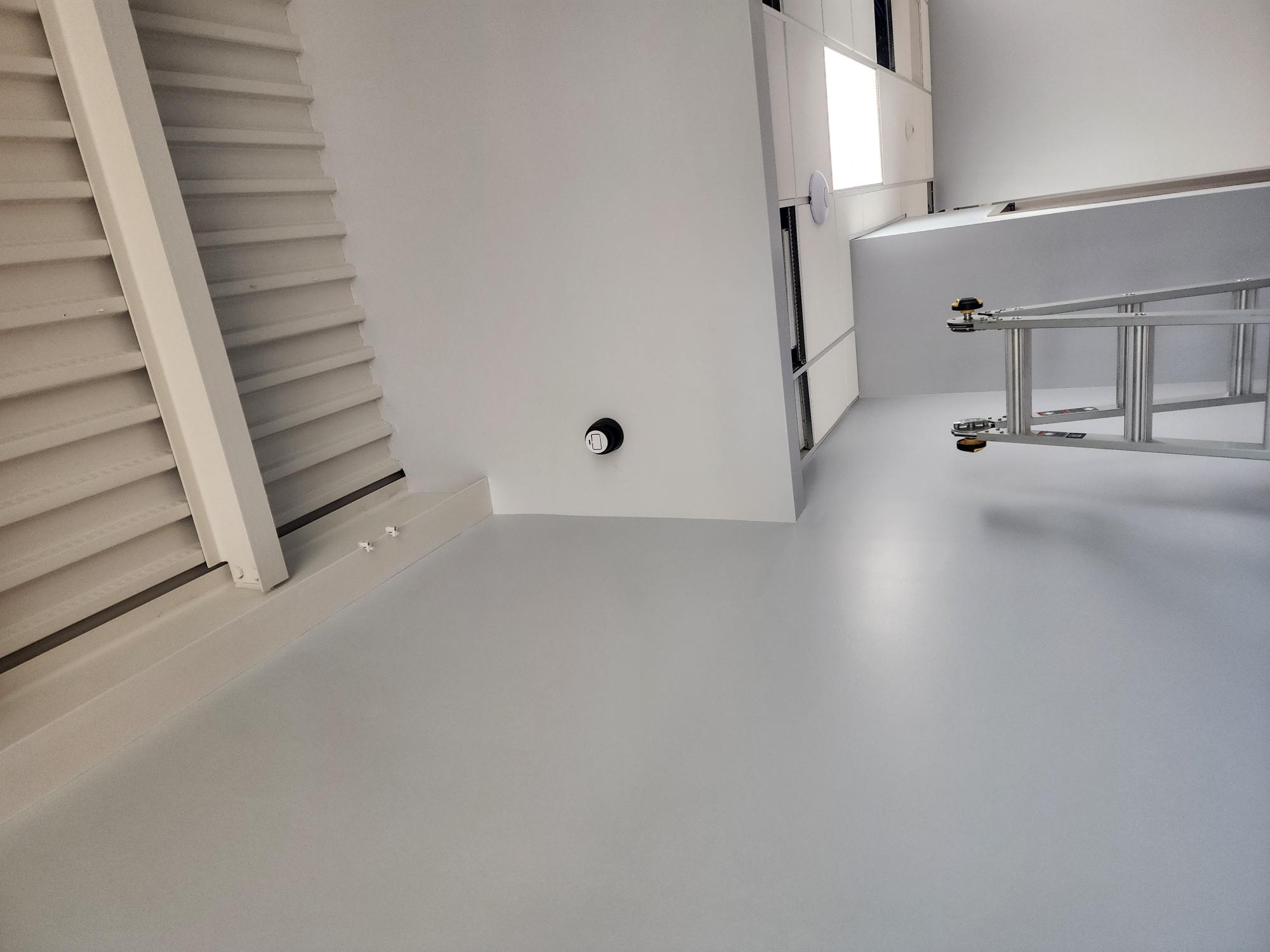 Interior room with light grey floor, white corrugated wall, a telescopic ladder, and a small mounted access point during network rack installation
