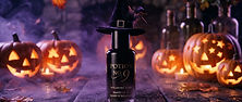A skincare bottle wearing a tiny black witch hat on a wooden table surrounded by glowing jack-o-lanterns, purple fog and drifting autumn leaves