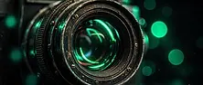 Close-up of a film camera lens reflecting green neon light in a dark studio