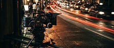 A film camera on a slider rail moving slowly toward a glowing city street at night, with motion blur lines showing the camera path