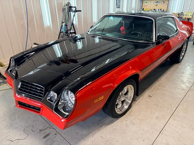 Red classic coupe with a black hood and roof, viewed from the front quarter inside a workshop.
