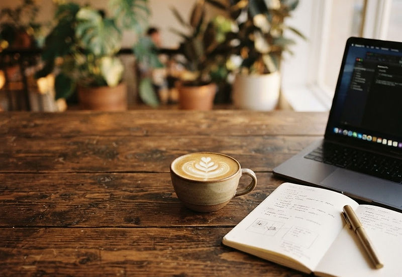 A latte, laptop, and notebook on a warm wood cafe table