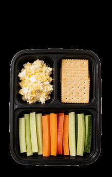Top-down view of a three-compartment meal tray with egg salad, crackers, and cucumber and carrot sticks