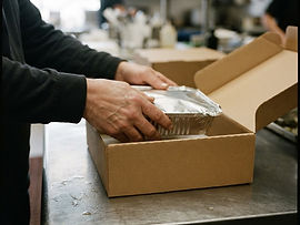 Hands sliding a wrapped, labeled meal tray into a delivery box