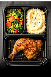 Top-down view of a three-compartment meal tray with roasted chicken, mashed potatoes, and vegetables