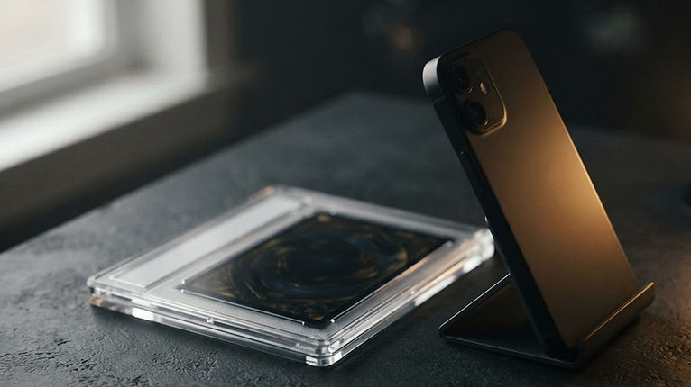 A smartphone on a small stand photographing a Pokémon card in a toploader on a plain dark background next to a window