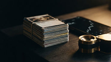 A stack of Pokémon cards on a table next to a phone showing recent sold prices and a magnifying loupe