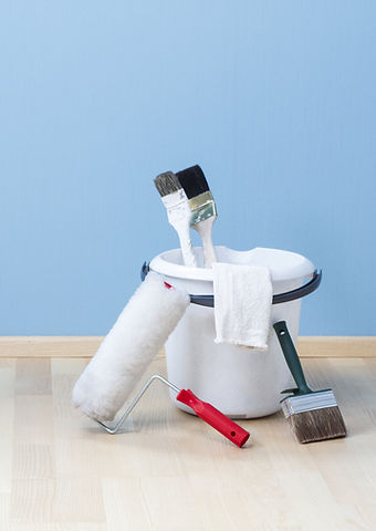 Pinceaux, rouleau et pot de peinture devant un mur bleu et un parquet clair