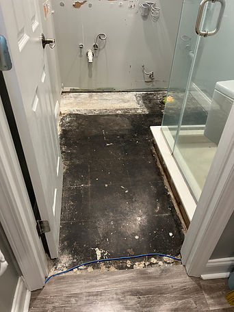 Bathroom floor with the old flooring removed beside a glass shower.