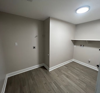 Laundry room with wood-look flooring, white baseboards, ceiling lighting and a wall shelf.