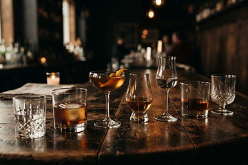 An array of spirit glasses on a dark wood bar in warm moody lighting