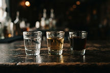 Three glasses of tequila ranging from clear blanco to amber añejo lined up on a dark surface