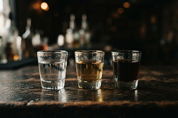 Three glasses of tequila ranging from clear blanco to amber añejo lined up on a dark surface