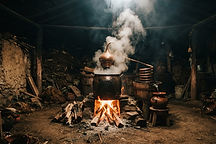 A traditional copper still producing mezcal with steam rising in a dim Oaxacan palenque
