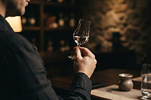 A copita glass of clear tequila held up to warm light to examine its color and clarity