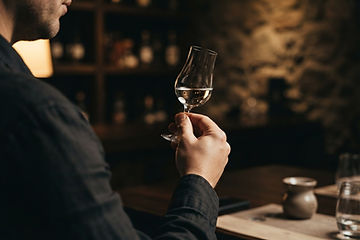 A copita glass of clear tequila held up to warm light to examine its color and clarity