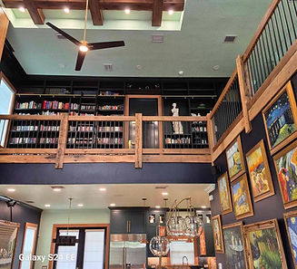 Double-height living space with a dark built-in mezzanine library, wood ceiling beams and kitchen below