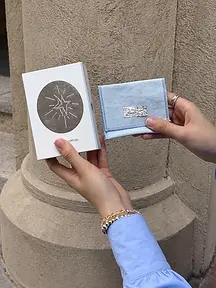 White printed jewelry box held beside a light blue fabric pouch with a silver card