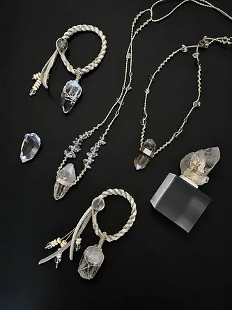 Crystal pendant necklaces, braided cord bracelets and loose crystal points arranged on a black background