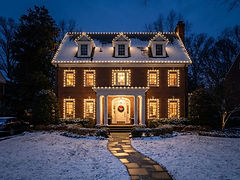 Two-story brick home with warm-white holiday lights outlining the rooflines, dormers, windows and porch columns — holiday lighting design inspiration