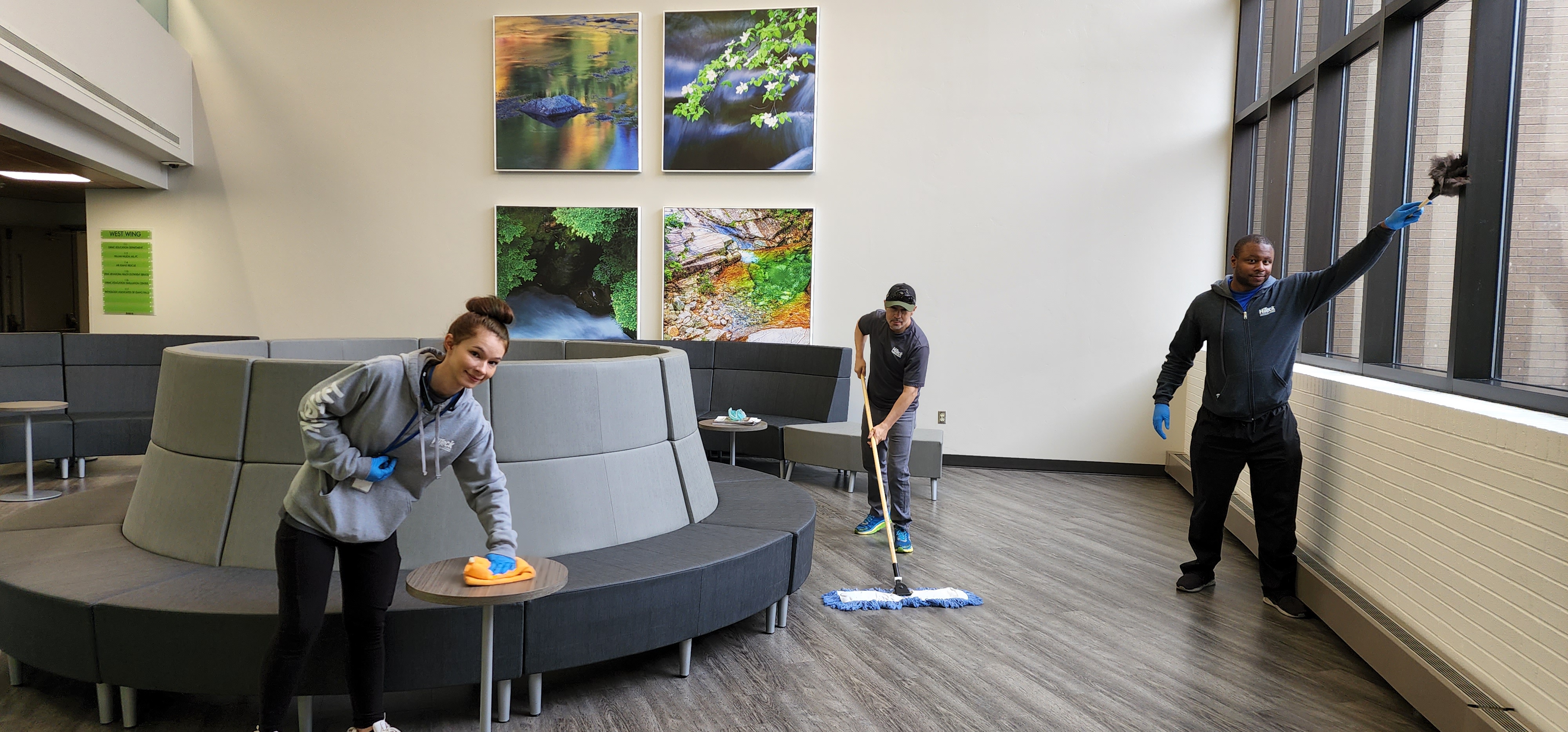 Three Hi-Teck crew members cleaning a medical building lobby, wiping tables, mopping, and dusting windows