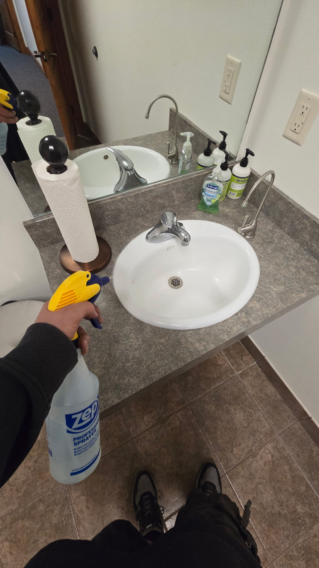 Hand holding a spray bottle pointed at a white restroom sink