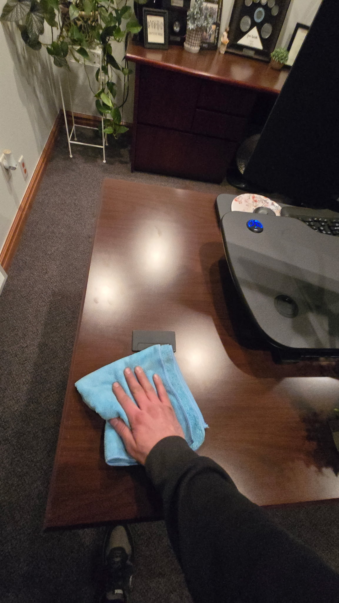Hand wiping a dark wooden desk surface with a blue microfiber cloth