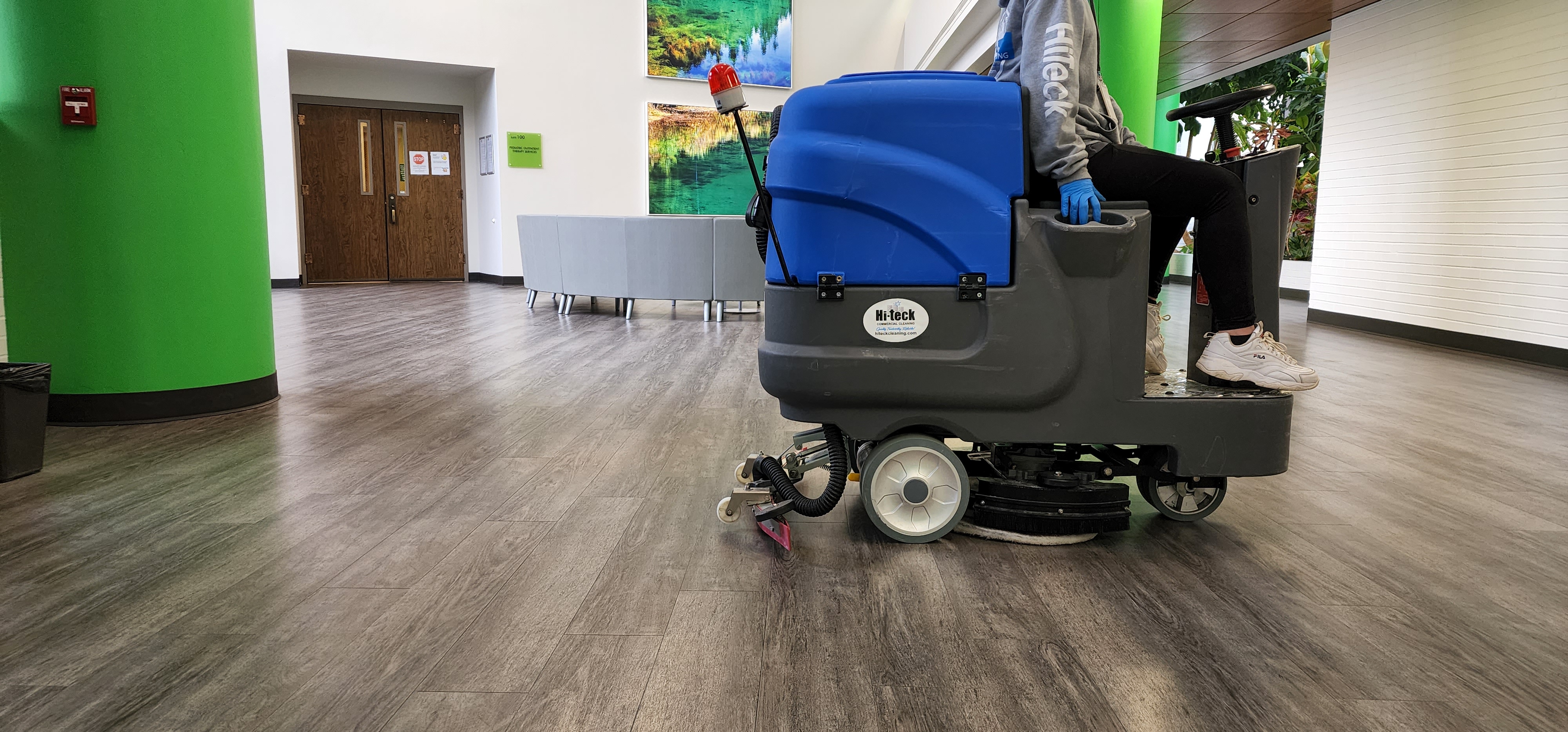 Hi-Teck crew member operating a ride-on floor scrubber down a commercial hallway