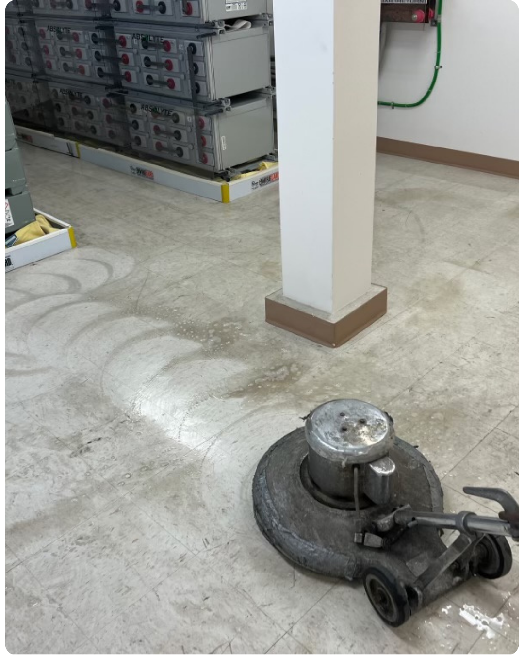 Commercial floor scrubber stripping a vinyl tile floor in an industrial room