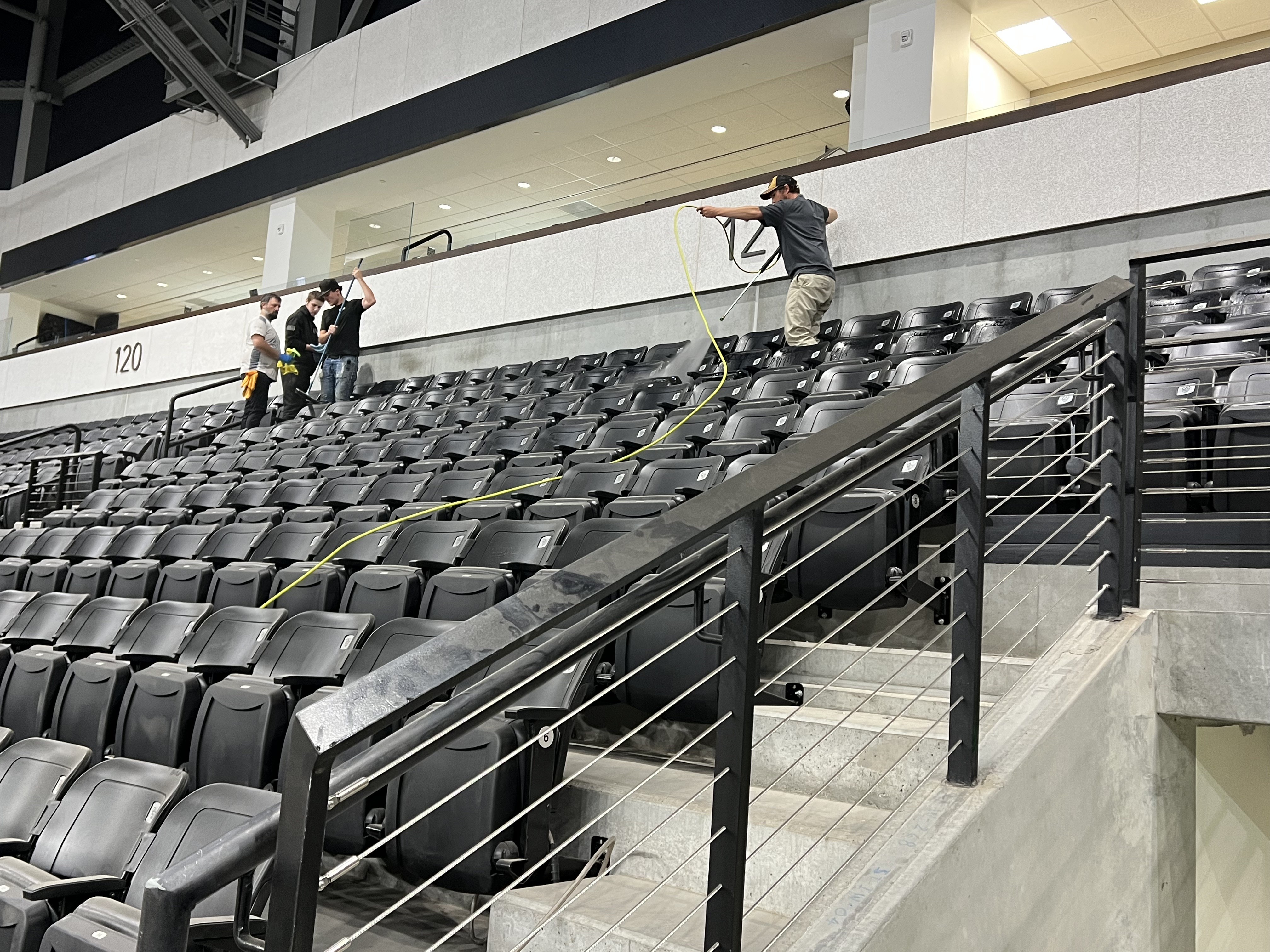 Hi-Teck crew member power-washing arena seats with a yellow hose while others wipe them down